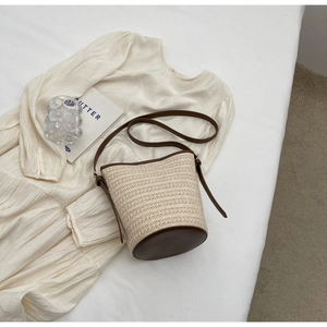 Detail of woven straw bucket bag with dark brown leather trim and adjustable strap