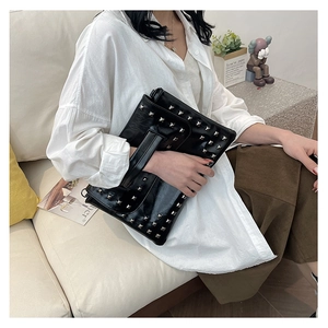 Dettaglio pochette in pelle nera lucida con borchie metalliche quadrate e cinturino a mano