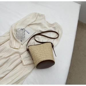 Detailed close-up of the straw bucket bag with dark brown leather trim and texture