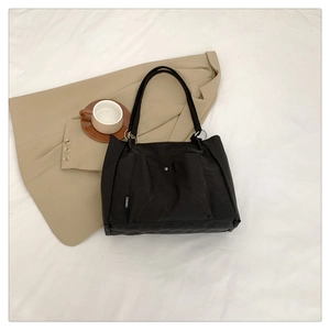 Detail of black canvas tote bag showing metal ring handles and front snap pocket