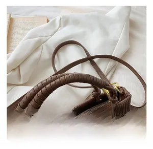 Detail of a brown pleated bucket bag featuring a unique hand-wrapped ring handle and gold hardware