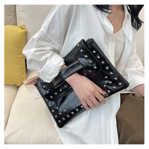 Dettaglio della pochette a busta in pelle nera lucida con borchie quadrate argentate e cinturino