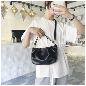 Fashionable black pleated cloud bag with gold chain strap shown on model in modern interior