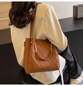 Brown quilted bucket bag with metal U-shaped handles carried by model in white suit