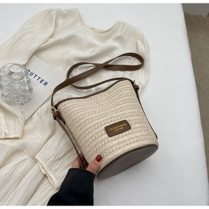 Detail of woven straw bucket bag with dark brown leather base and branded patch