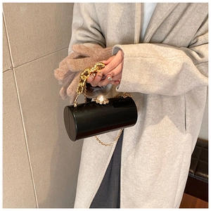 Detail view of black acrylic cylinder bag with gold chain and pearl clasp accents