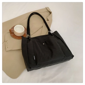 Detail shot of the black canvas tote bag showing the front pocket and brand woven label