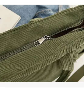 Detailed macro view of the silver metal zipper on the green corduroy tote bag surface