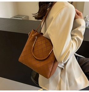 Detailed view of brown quilted leather bucket bag with metal handle on female model