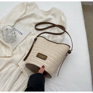 Detail of woven straw bucket bag with brown leather trim on white pleated dress