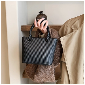 Detail of black pleated tote bag showing vertical stripe texture and metal rings on handles