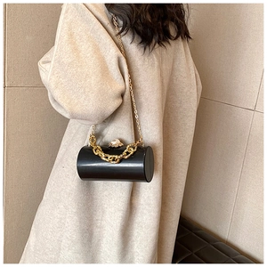 Detail view of black acrylic cylinder clutch with pearl clasp and gold chain strap