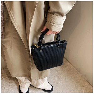 Detail of black pleated bucket bag with spiral woven handle and gold zipper hardware