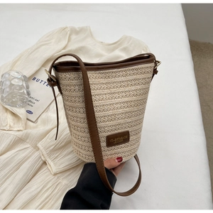 Detail of woven straw bucket bag with dark brown leather trim and subtle branding logo