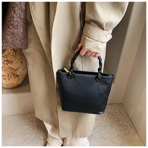 Detail of black pleated bucket bag with vertical ridges and knotted handle design