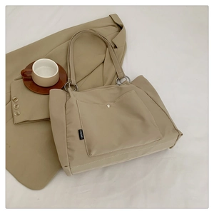 Detail of beige nylon tote bag featuring metal ring handle attachment and front snap pocket