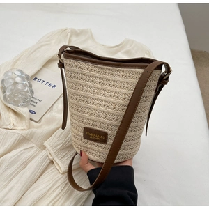 Detailed close-up of a woven straw bucket bag with brown leather trim and brand leather patch