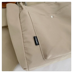Detailed close-up of side pocket and silver hardware on a khaki nylon tote bag