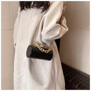 Detail of black cylindrical evening bag with gold chain and large pearl clasp on beige coat