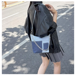 Detail view of a patchwork denim shoulder bag with silver chain strap and leather belt