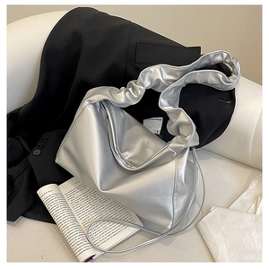 Detailed view of metallic silver hobo bag with pleated shoulder strap on a white sofa