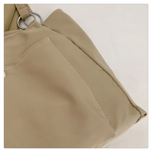 Detail of khaki tote bag showing nylon texture, white stitching, and metal ring hardware