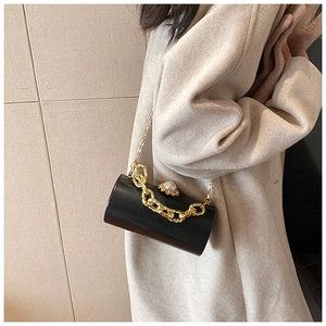 Close-up of a black acrylic cylinder clutch bag with pearl clasp and gold chain detail