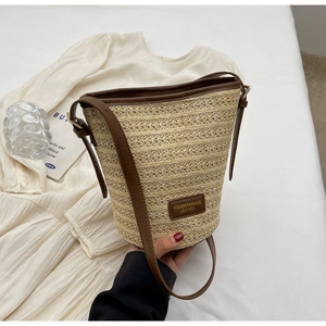 Detail shot of the woven straw bucket bag showing fine texture and brown leather trim