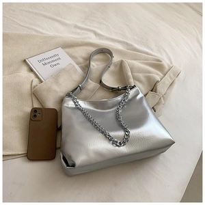 Close-up of a silver hobo bag with thick metal chain and sleek leather strap on soft fabric
