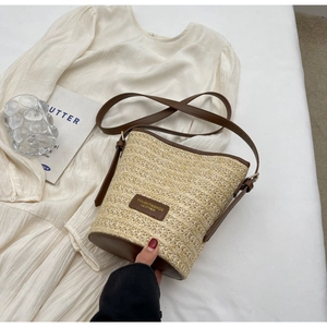 Detail of woven straw bucket bag with brown leather trim and adjustable shoulder strap