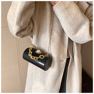 Detail of a black acrylic cylinder clutch bag with gold chain and large pearl clasp decoration
