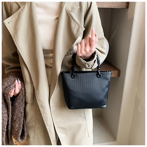 Detailed view of black pleated bucket bag with knotted leather handle on a beige trench coat