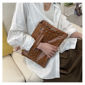 Dettaglio della pochette in pelle marrone con borchie quadrate argentate e cinturino