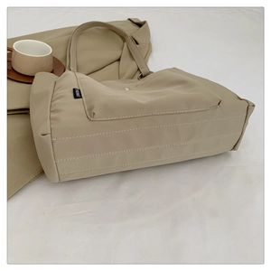 Detail of beige nylon tote bag with front pocket and quilted bottom stitching