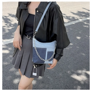 Detail of color-block denim crossbody bag with silver metal chain on a street background