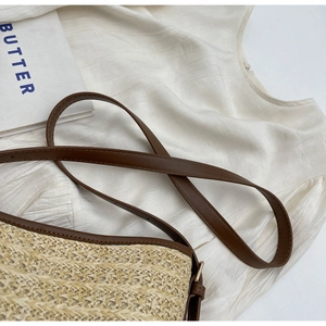 Detail of woven straw bucket bag with dark brown leather trim and golden metal buckle