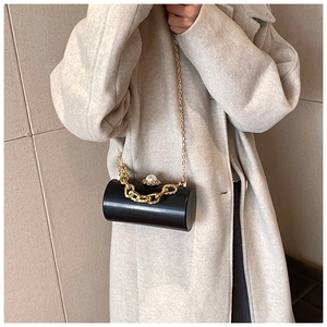 Detail of a black cylinder clutch with pearl clasp and gold chain over a beige coat