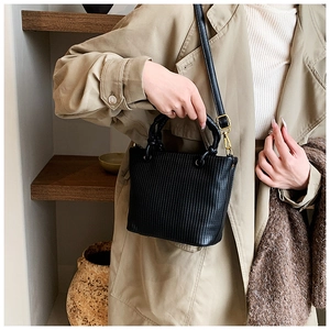 Detail shot of vertical pleated texture and gold metal ring on a black bucket bag