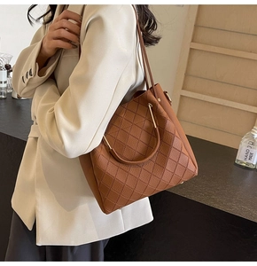 Detail of a brown quilted bucket bag with golden circular metal handles and shoulder strap