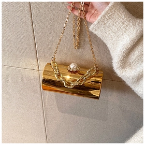 Detail of golden acrylic mirror cylinder bag with pearl clasp and dual metal chains