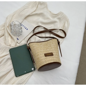 Close-up of woven straw bucket bag with brown leather trim and shoulder strap detail