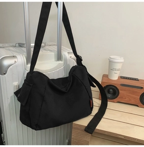 Détail du sac bandoulière en toile noire avec sangle réglable et poche sur valise