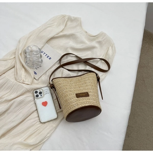 Top-down view of woven straw bucket bag with brown leather trim on a summer dress