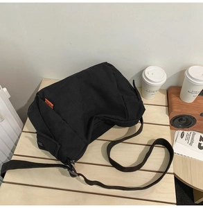 Détail d'un sac bandoulière en toile noire avec étiquette orange et sangle réglable
