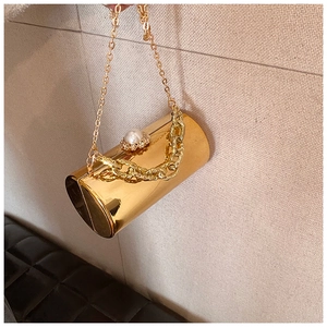 Detail of a golden cylinder evening bag with mirror finish and pearl top decoration