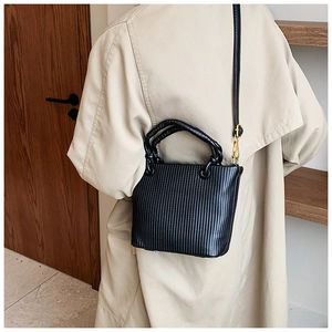 Detail of black pleated bucket bag with twisted handle and gold hardware on beige coat