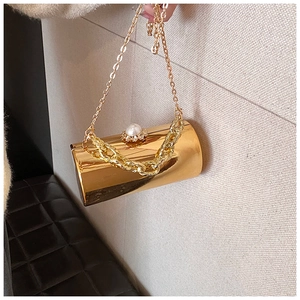 Detailed macro of golden mirror cylinder evening bag featuring pearl rhinestone clasp detail