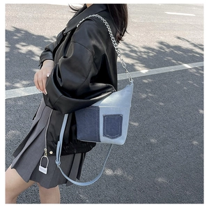 Detail of denim patchwork bucket bag with silver chain and leather strap on model