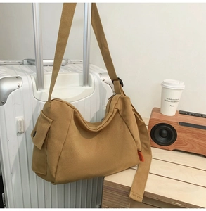 Détail du sac bandoulière en toile kaki avec poche latérale et sangle sur une valise