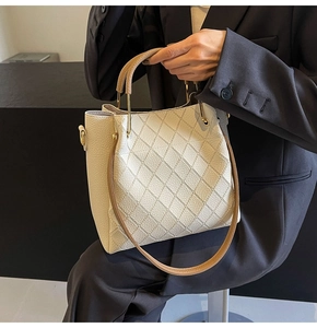 Detailed view of beige bucket bag featuring quilted leather texture and metal ring handle